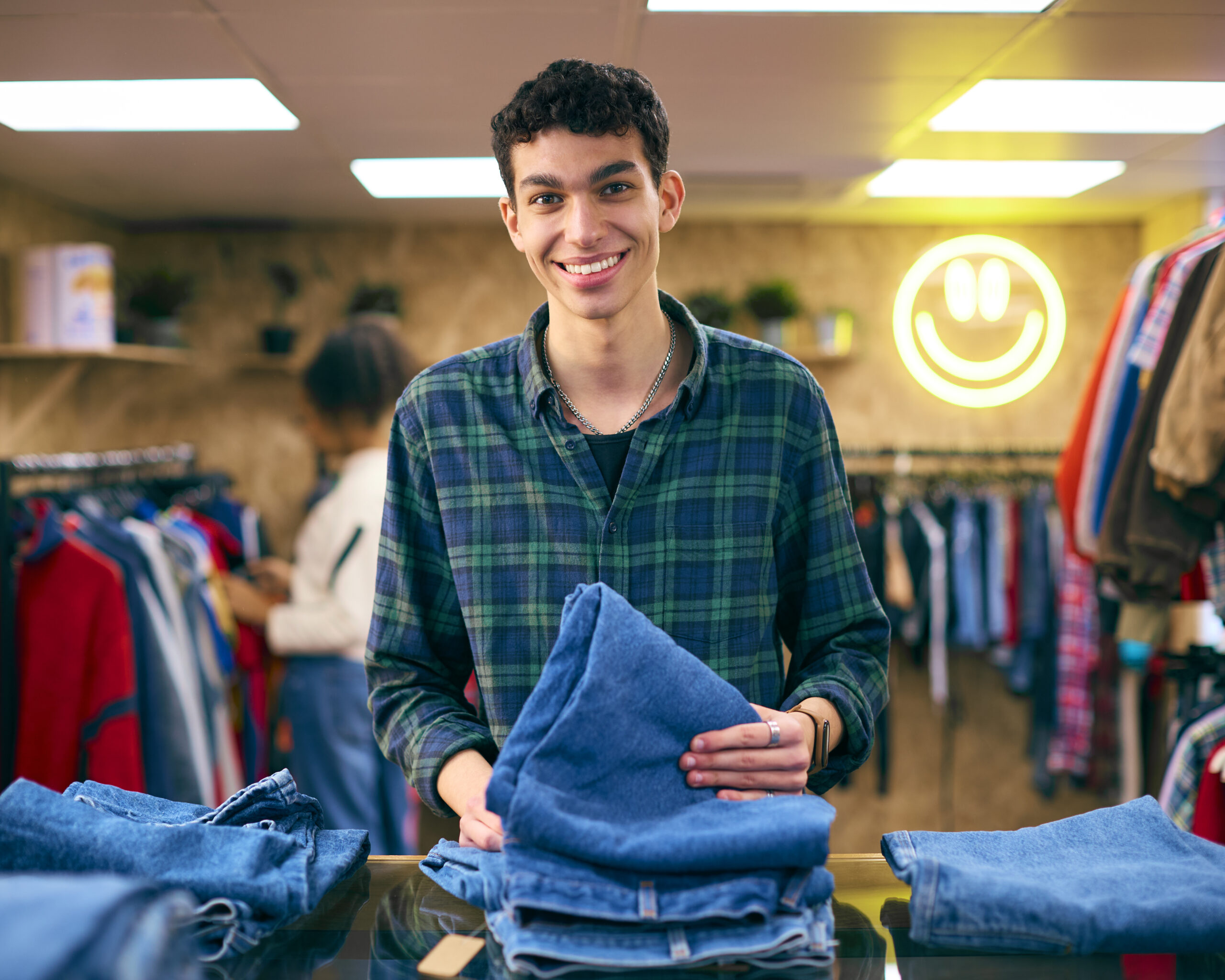 Portrait Of Male Sales Assistant Or Customer Sorting And Looking At Jeans In Fashion Store