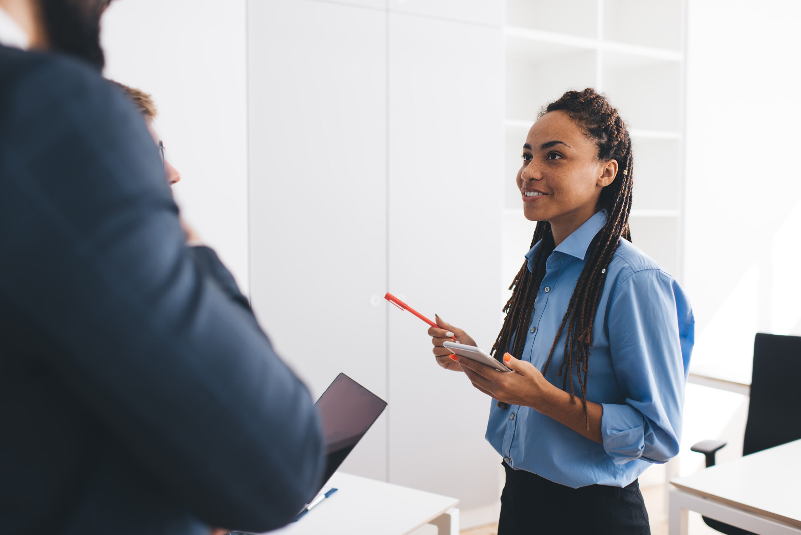 African American female employee with cellular gadget communicate with colleagues during time for together briefing in corporate office, secretary with mobile device discussing business strategy