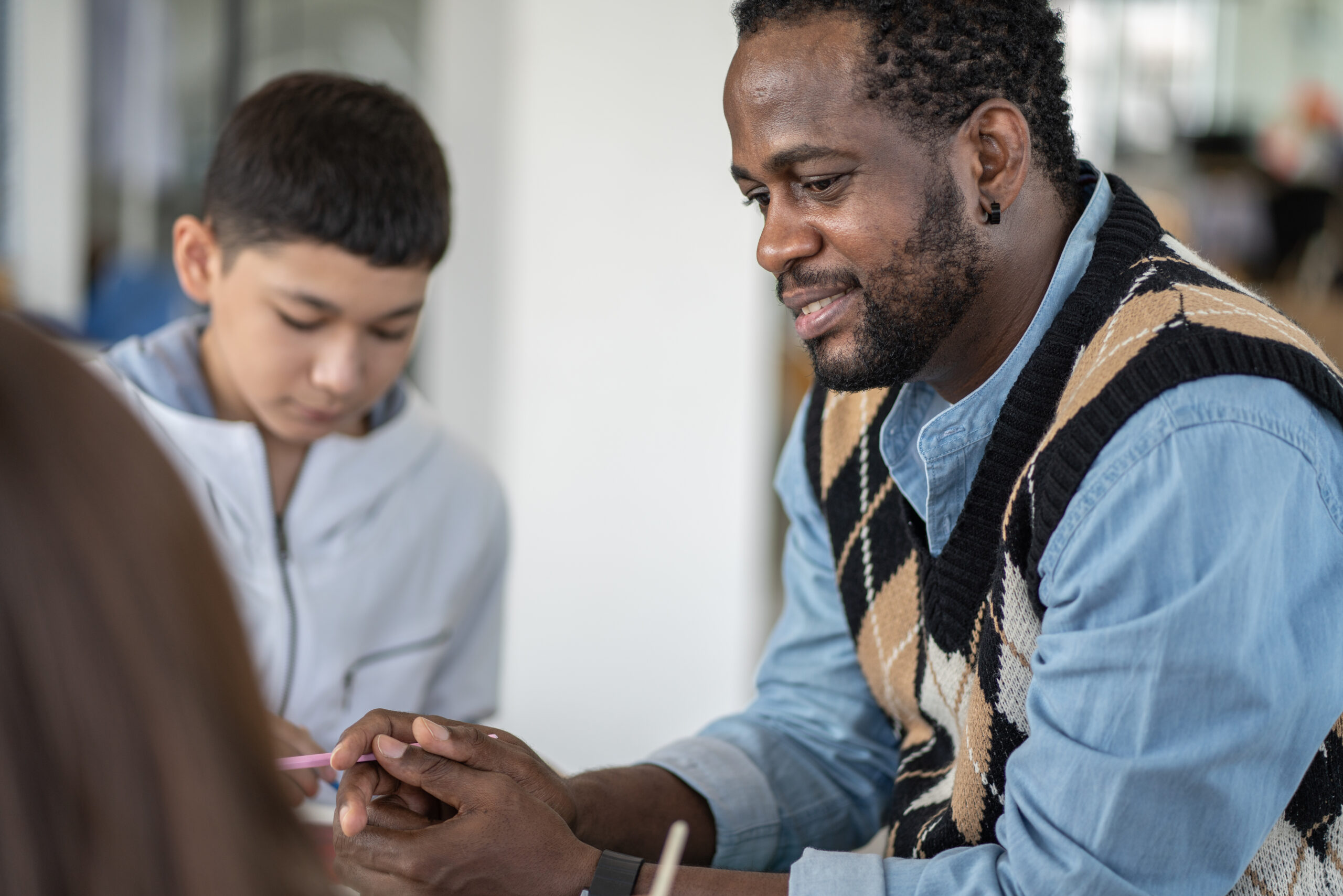 Smiling African American teacher looking and taking care of student activity in the classroom at school. Satisfied man happy with children.